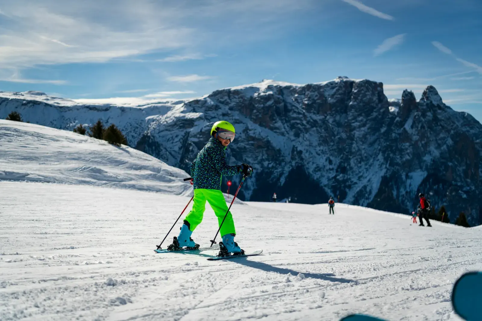 Bambino con casco e maschera che scia su una pista facile, con le Dolomiti sullo sfondo