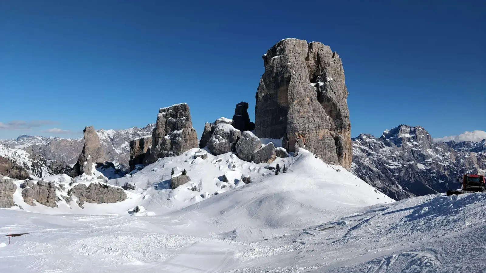 Le Cinque Torri innevate sopra la pista, con un gatto delle nevi a destra
