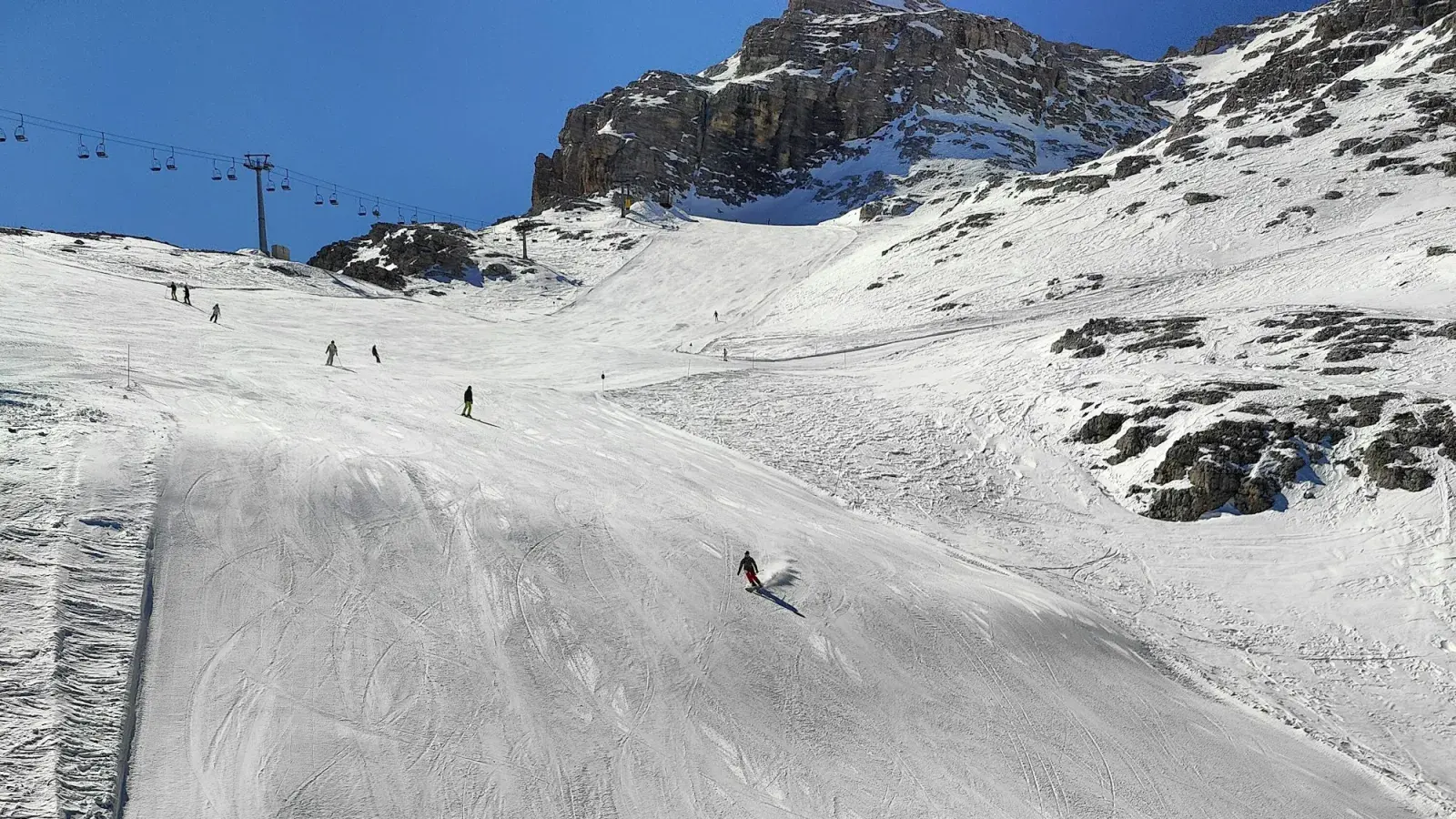 Sciatori su una pista battuta della Tofana a Cortina, con la seggiovia e le rocce sullo sfondo
