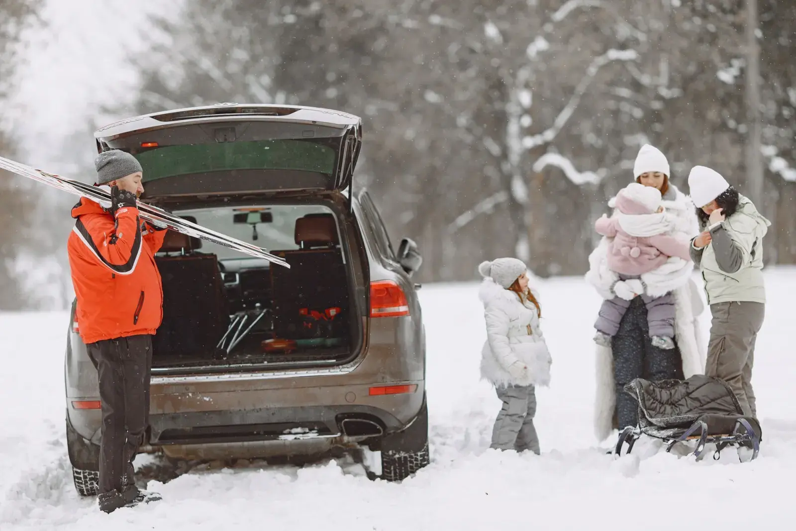 Una famiglia sulla neve accanto a un'auto con il bagagliaio aperto, il papà con gli sci in spalla