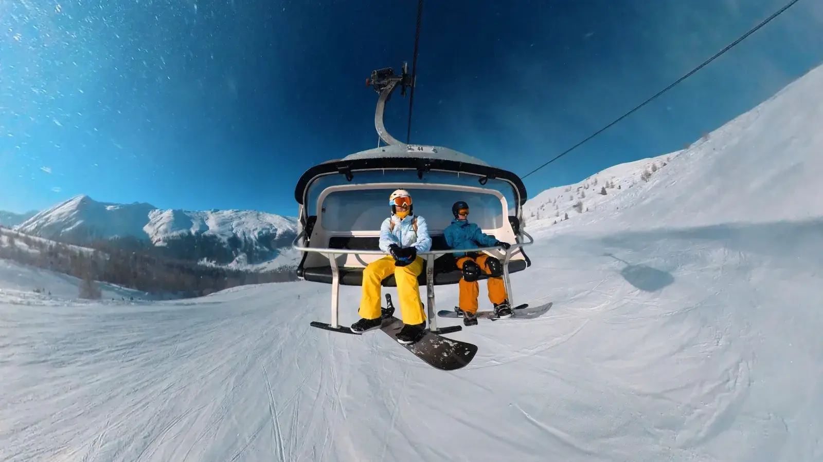 Due snowboarder con casco in seggiovia sopra una pista di Livigno