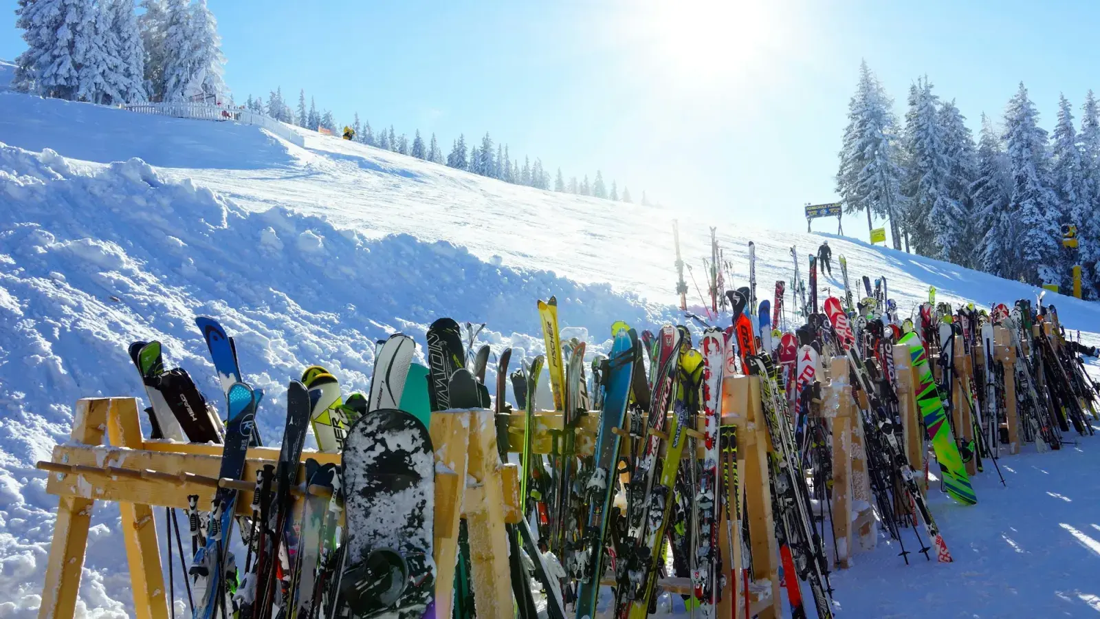 Sci e snowboard appoggiati a una rastrelliera di legno sulla neve, in una giornata di sole