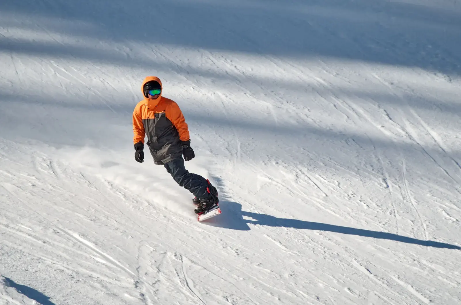 Snowboarder con casco che scende su una pista al sole